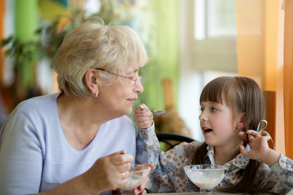 Grandchild sharing yogurt with grandmother